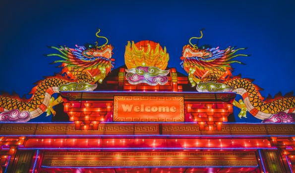 Colorful illuminated dragon lanterns at a night festival with a welcoming sign.