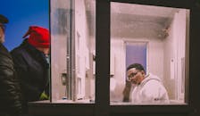 晚上，一名身穿白色连帽衫的男子若有所思地在玻璃隔间里与人互动