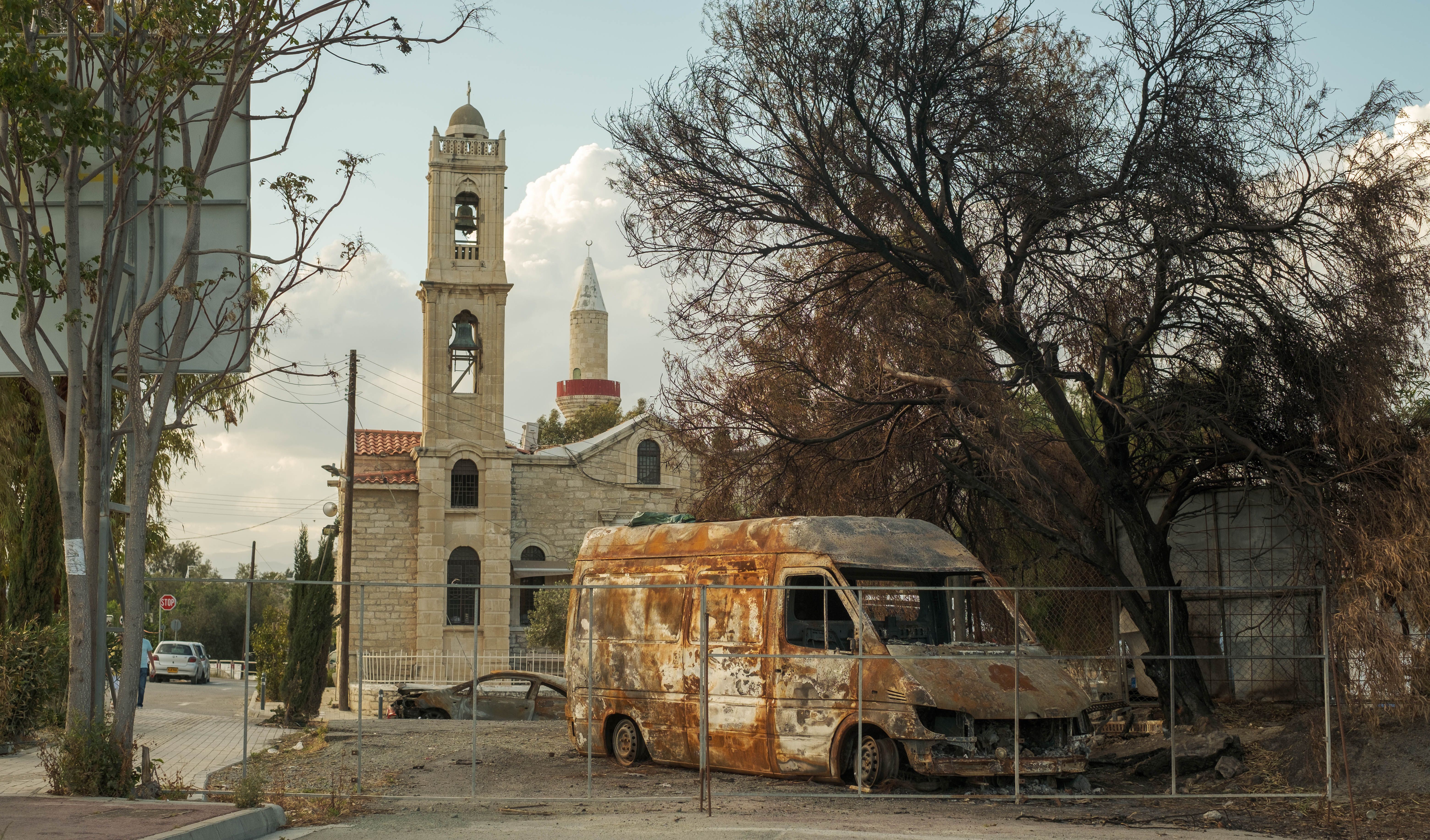 Rusty van in front of a historic church with mosque in the background, creating a contrast of decay and heritage.