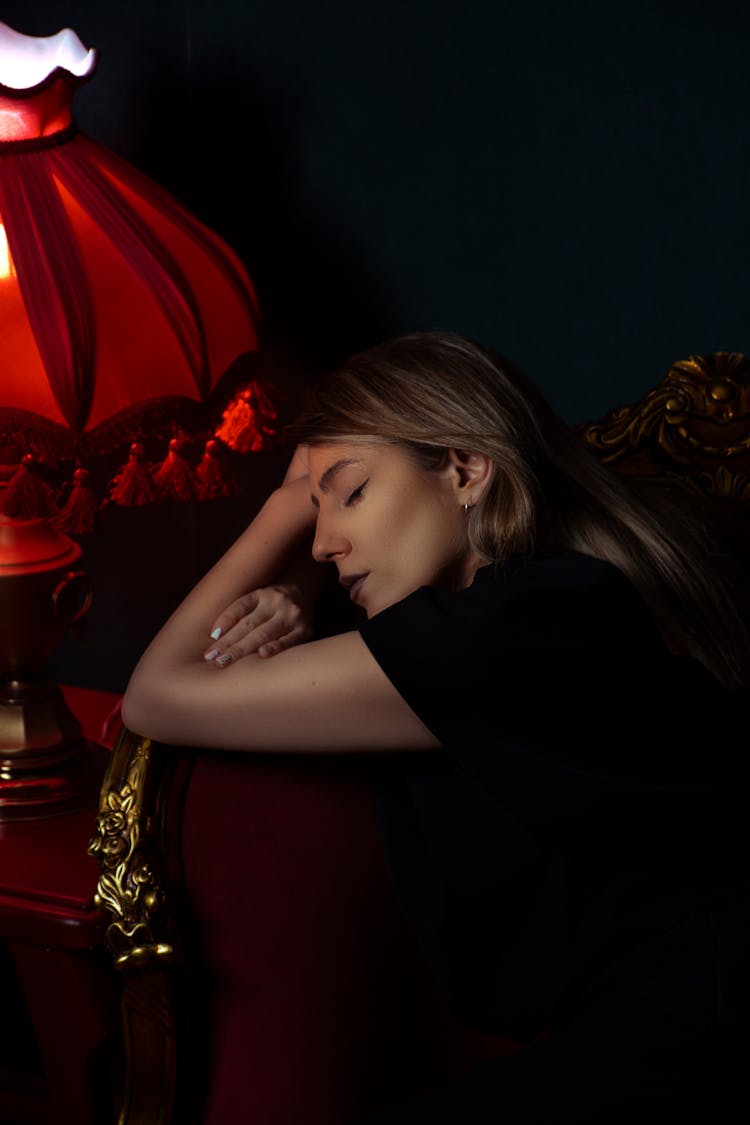 Young Woman Sleeping On Table Near Retro Lamp