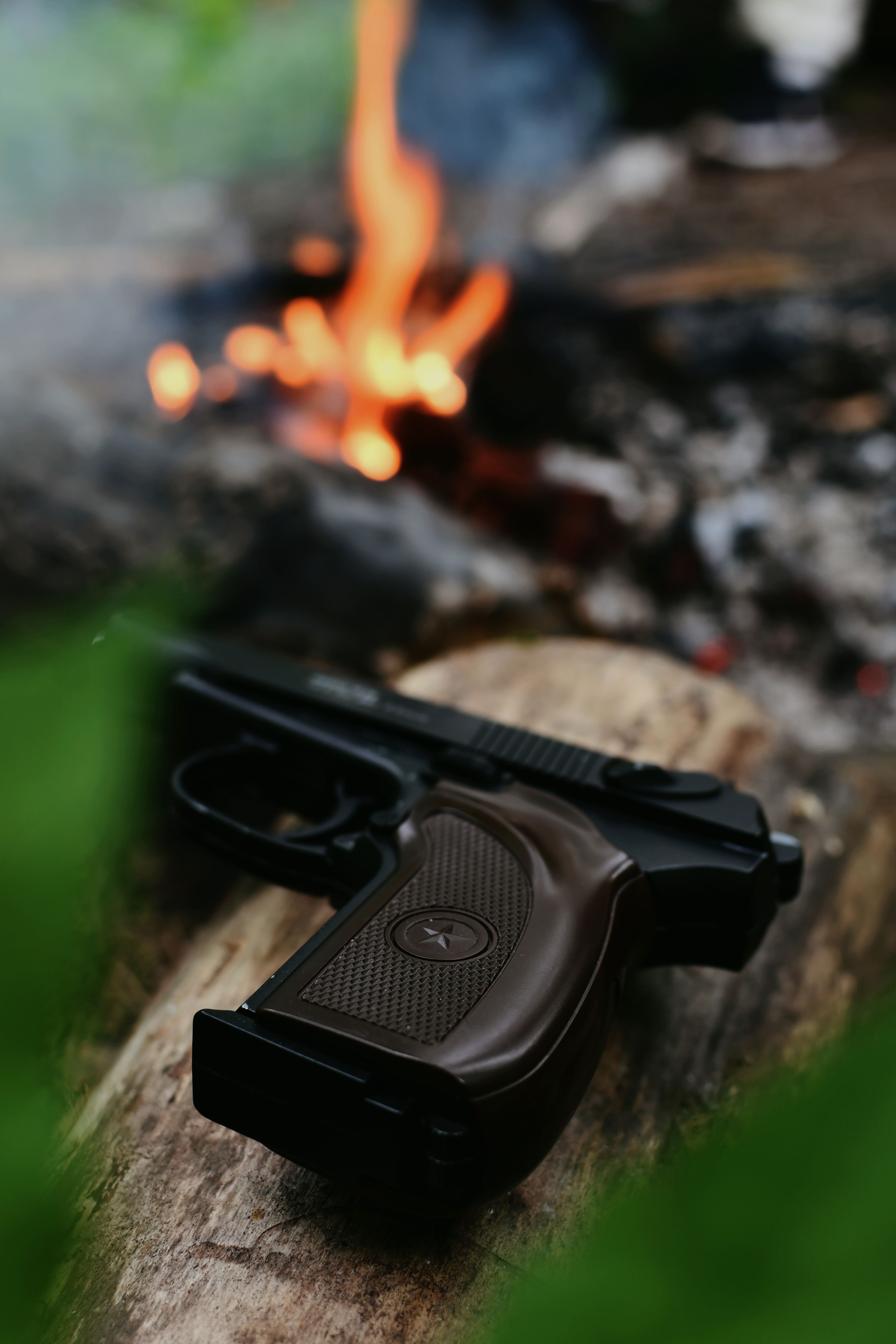 Makarov pistol on a wooden log with blurred campfire in the background, creating an outdoor camping scene.