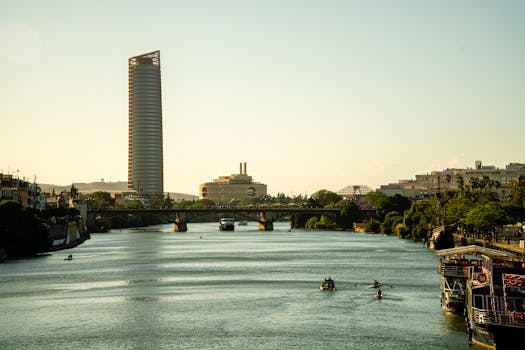 Tranquil view of Seville's river, modern bridges, and city skyline at sunset.