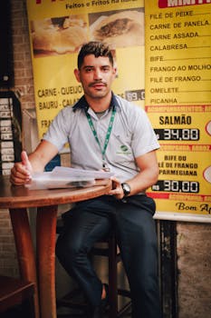 Man sitting at a cafe table, holding a folder with a menu visible behind him.