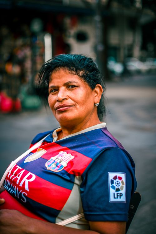 Free Portrait of a woman in a soccer jersey on a lively city street with a confident expression. Stock Photo
