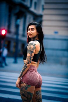 Fashionable woman with tattoos crossing a city street in the evening, showcasing urban style.