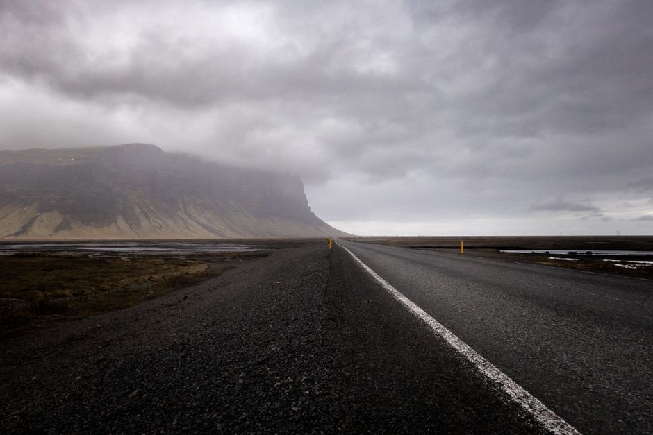 Desolate road disappearing into a foggy mountain landscape under an overcast sky.