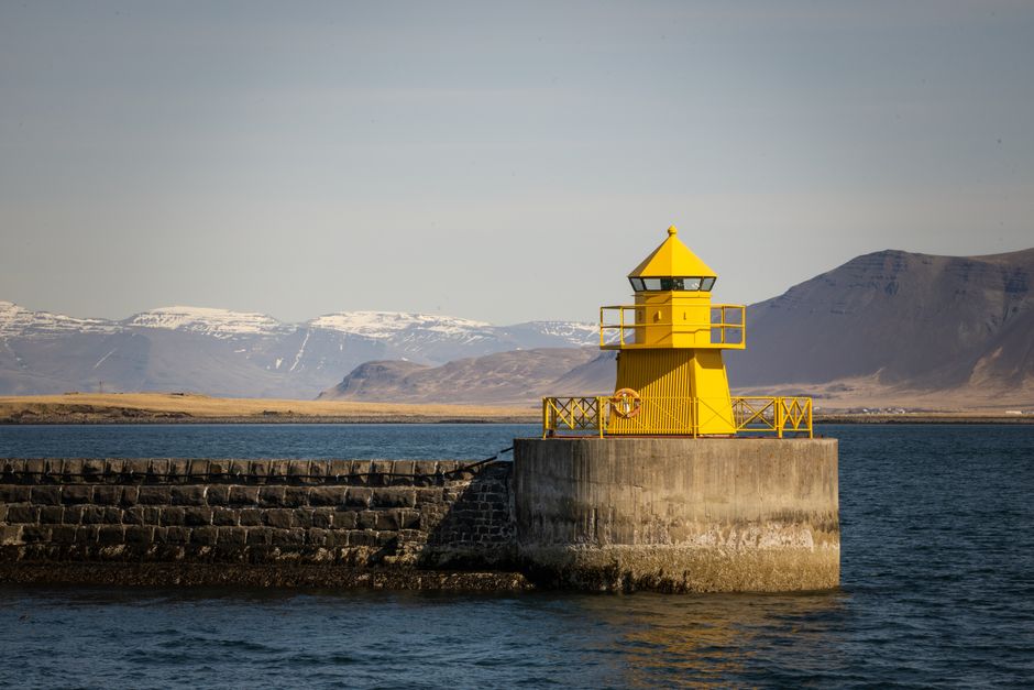 Eye-catching yellow lighthouse near a serene coastline and mountains.