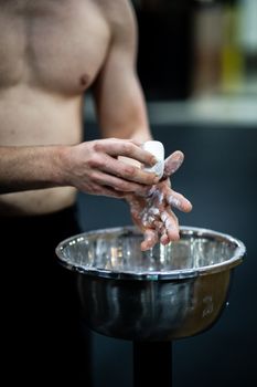 A fit man applying chalk on his hands, preparing for a weightlifting session in an indoor gym.