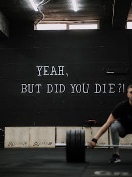 Man lifting weights in a gym with motivational quote on wall. Perfect for fitness inspiration.