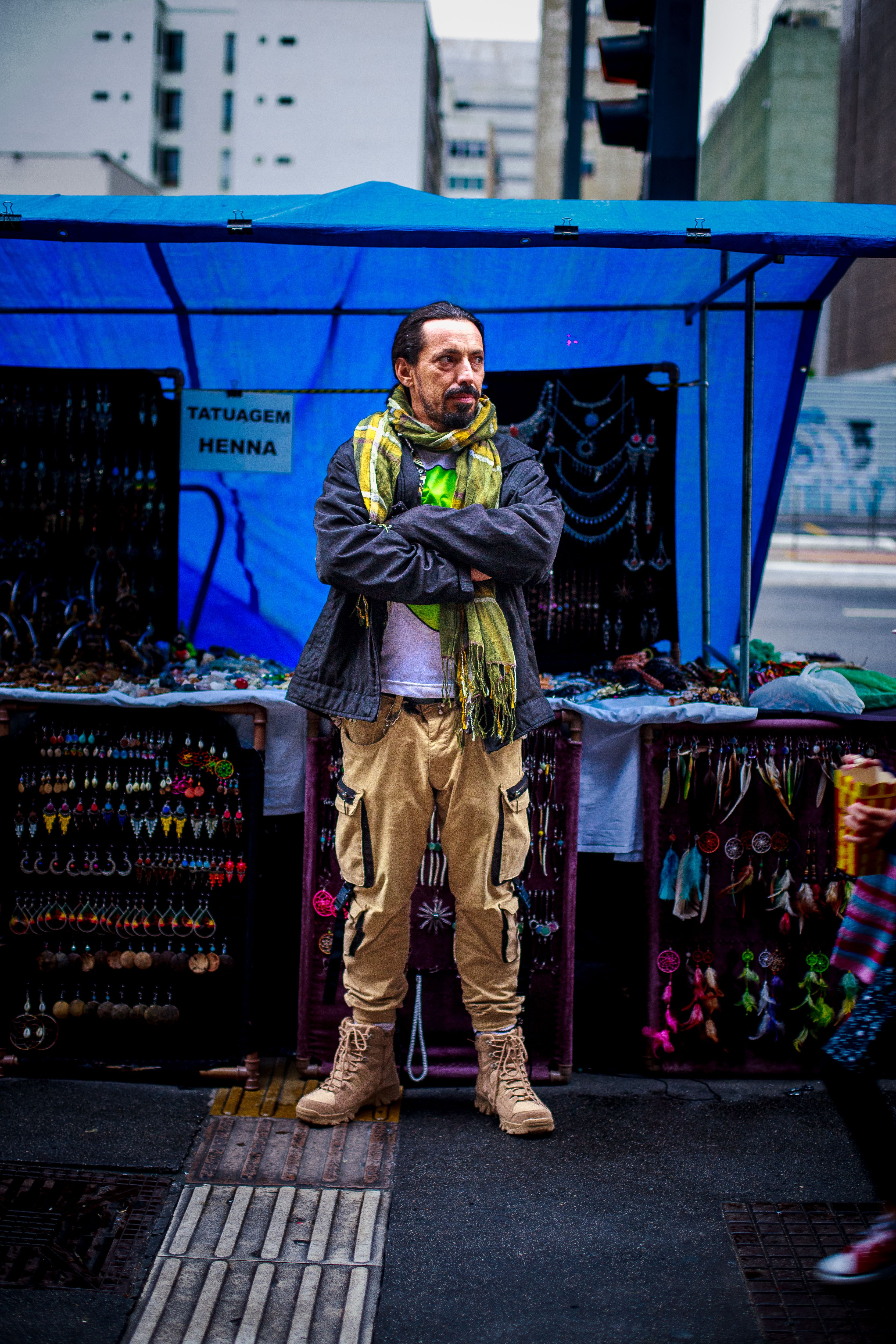 A man stands confidently at his accessories stall in an urban market setting.
