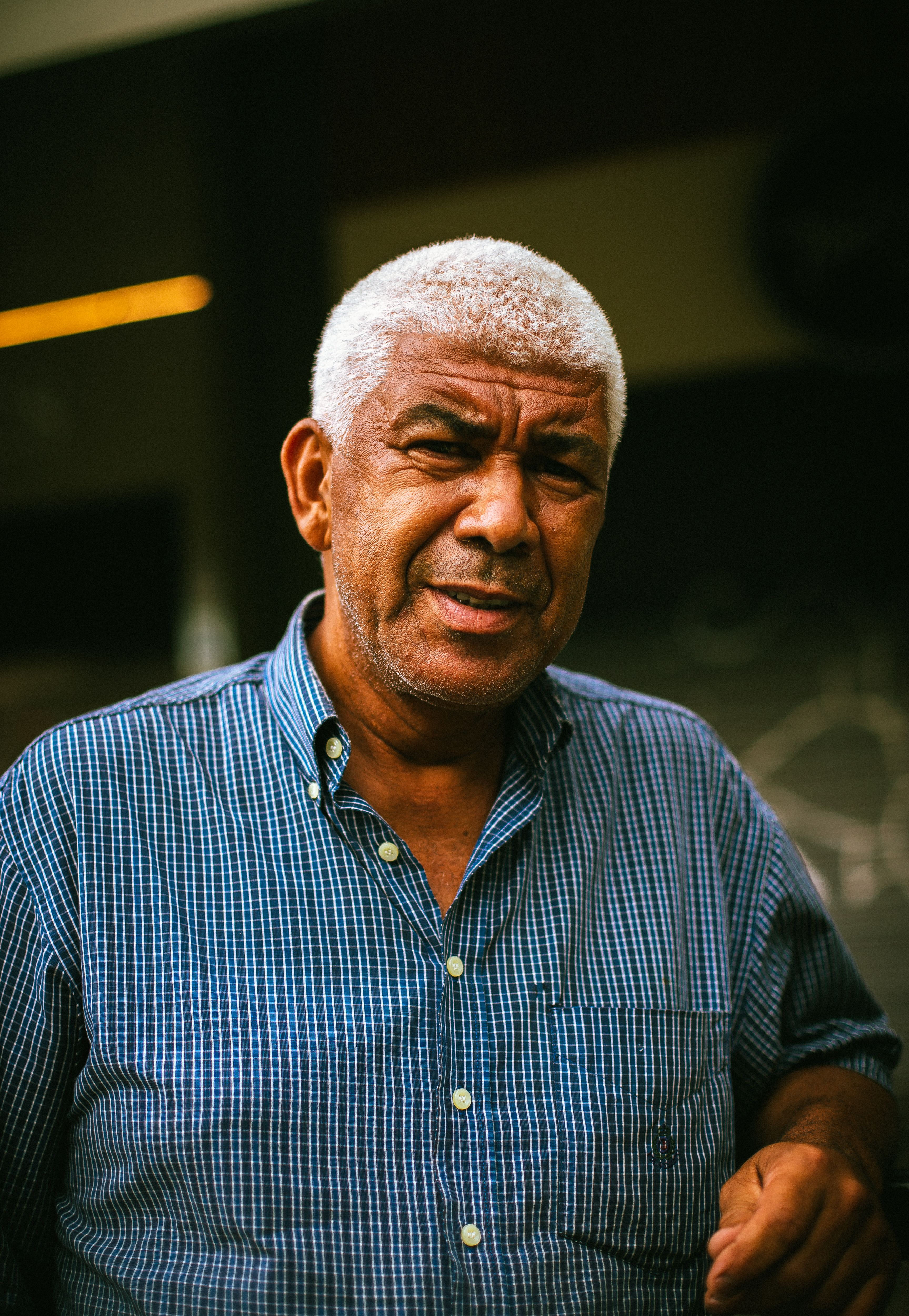 A thoughtful portrait of an elderly man with gray hair wearing a plaid shirt, captured outdoors.