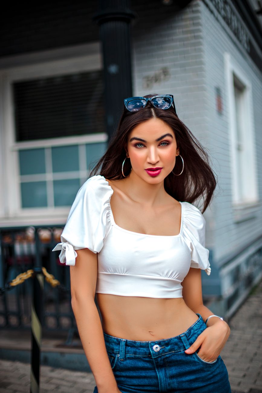 Stylish woman wearing a white top and jeans poses confidently in an urban setting, embodying modern fashion.