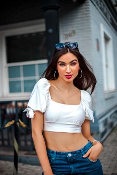 Stylish woman wearing a white top and jeans poses confidently in an urban setting, embodying modern fashion.