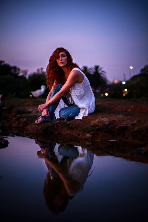 Redhead Woman Sitting on Lakeshere at Dusk