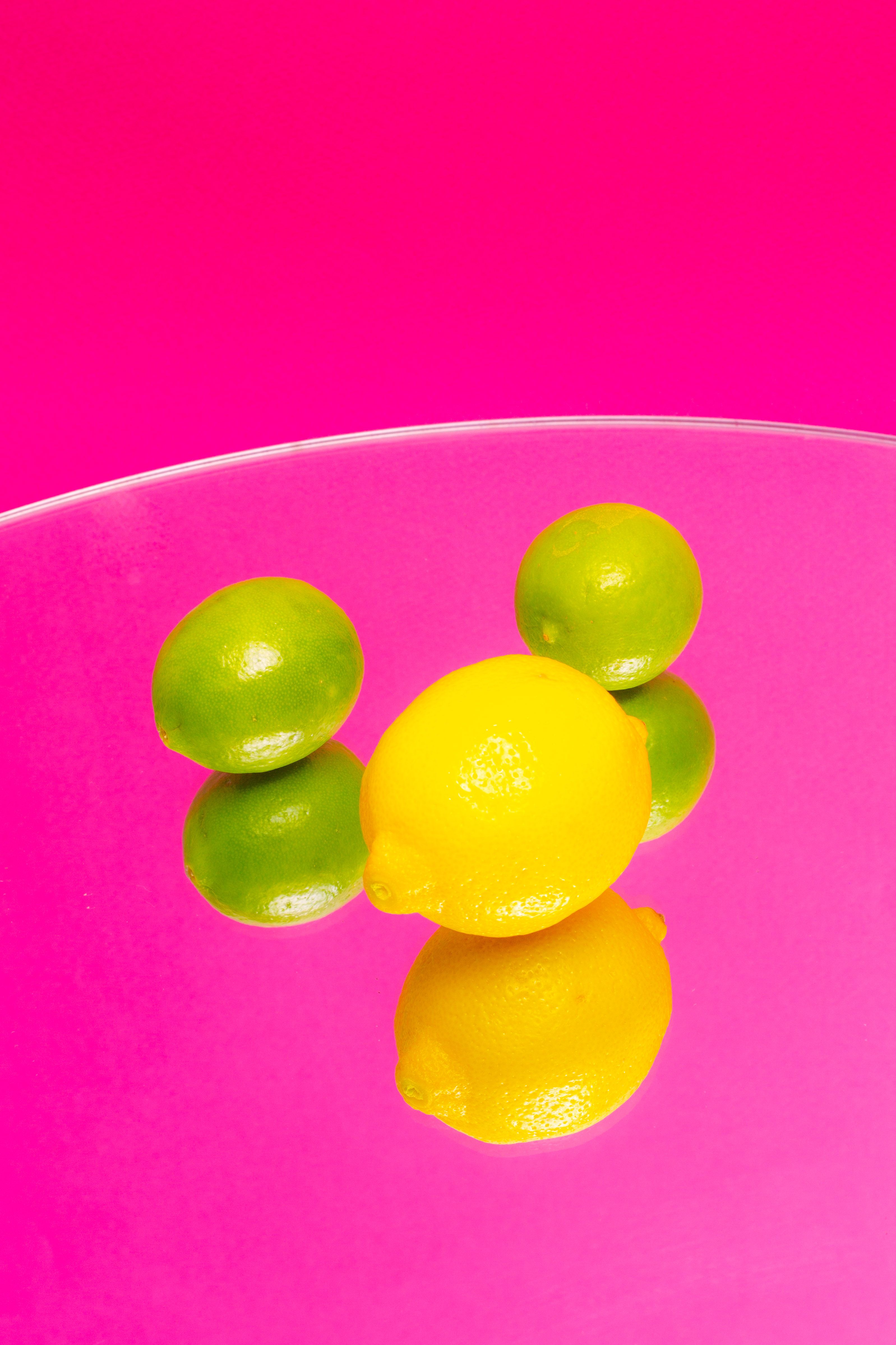 Fresh lemons and limes with reflections on a bright pink background create a vibrant composition.