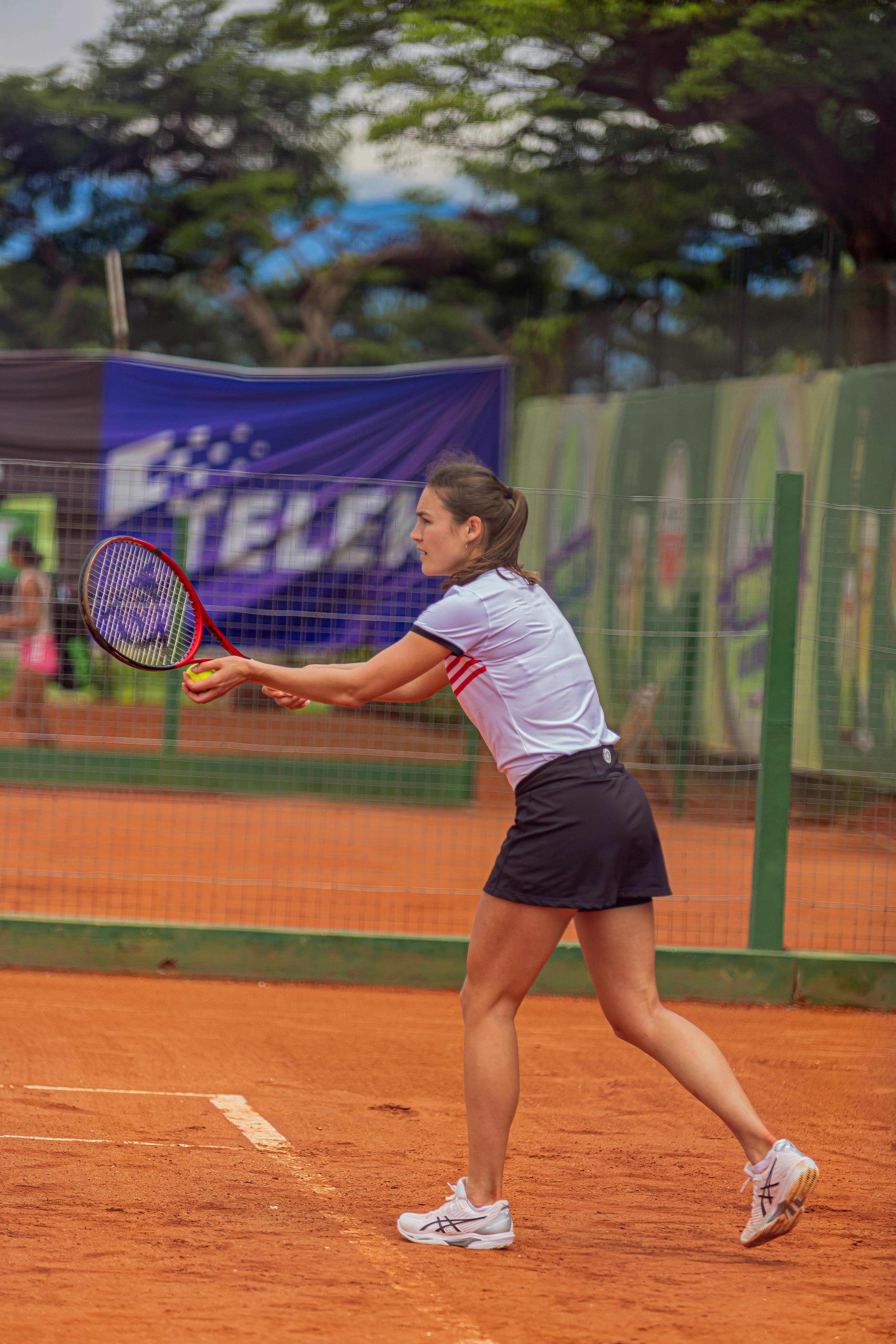 Focused female tennis player swings racket during a game on a clay court.