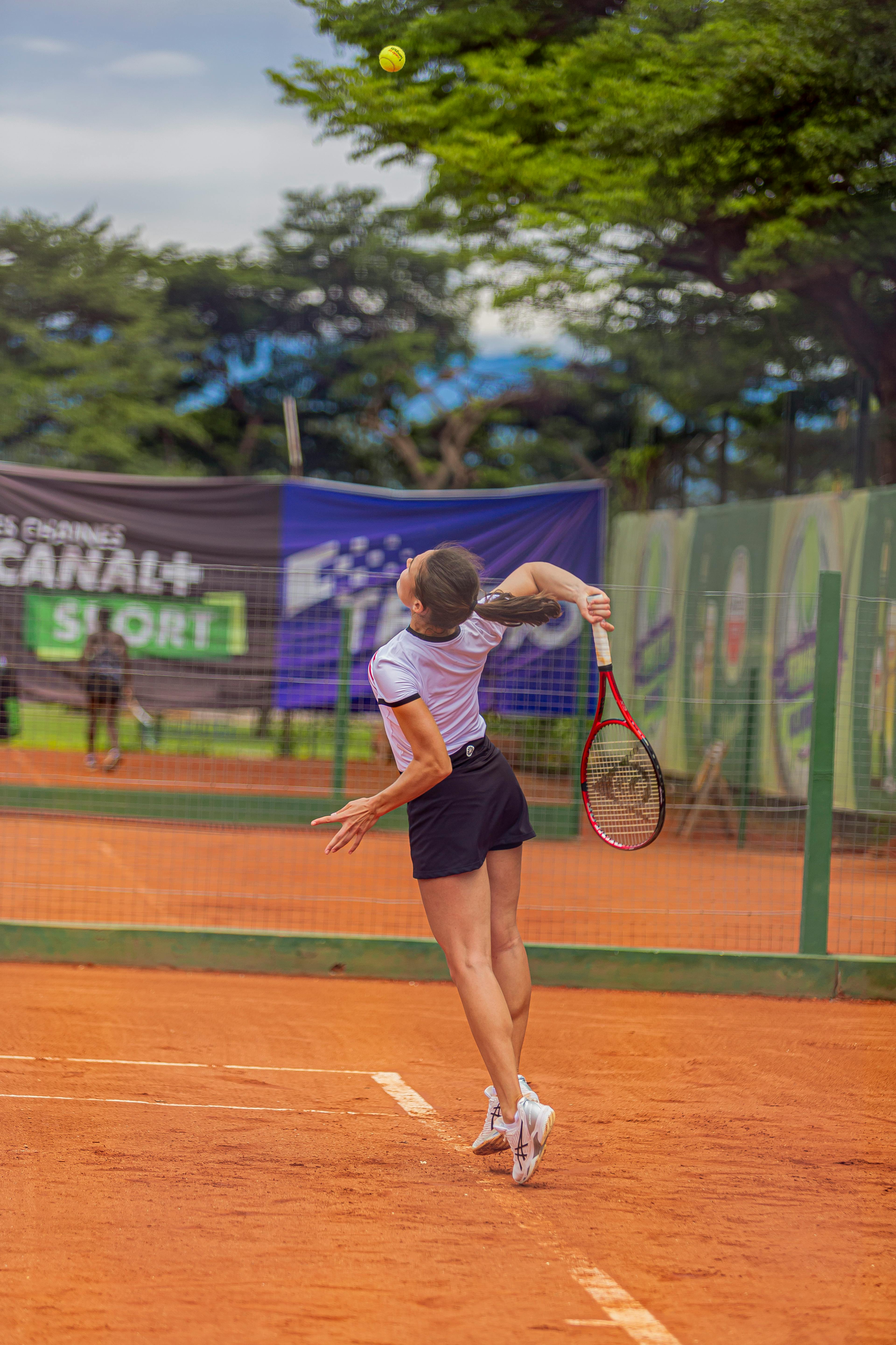Atleta jovem sacando em quadra de saibro durante uma semifinal de tênis ao ar livre