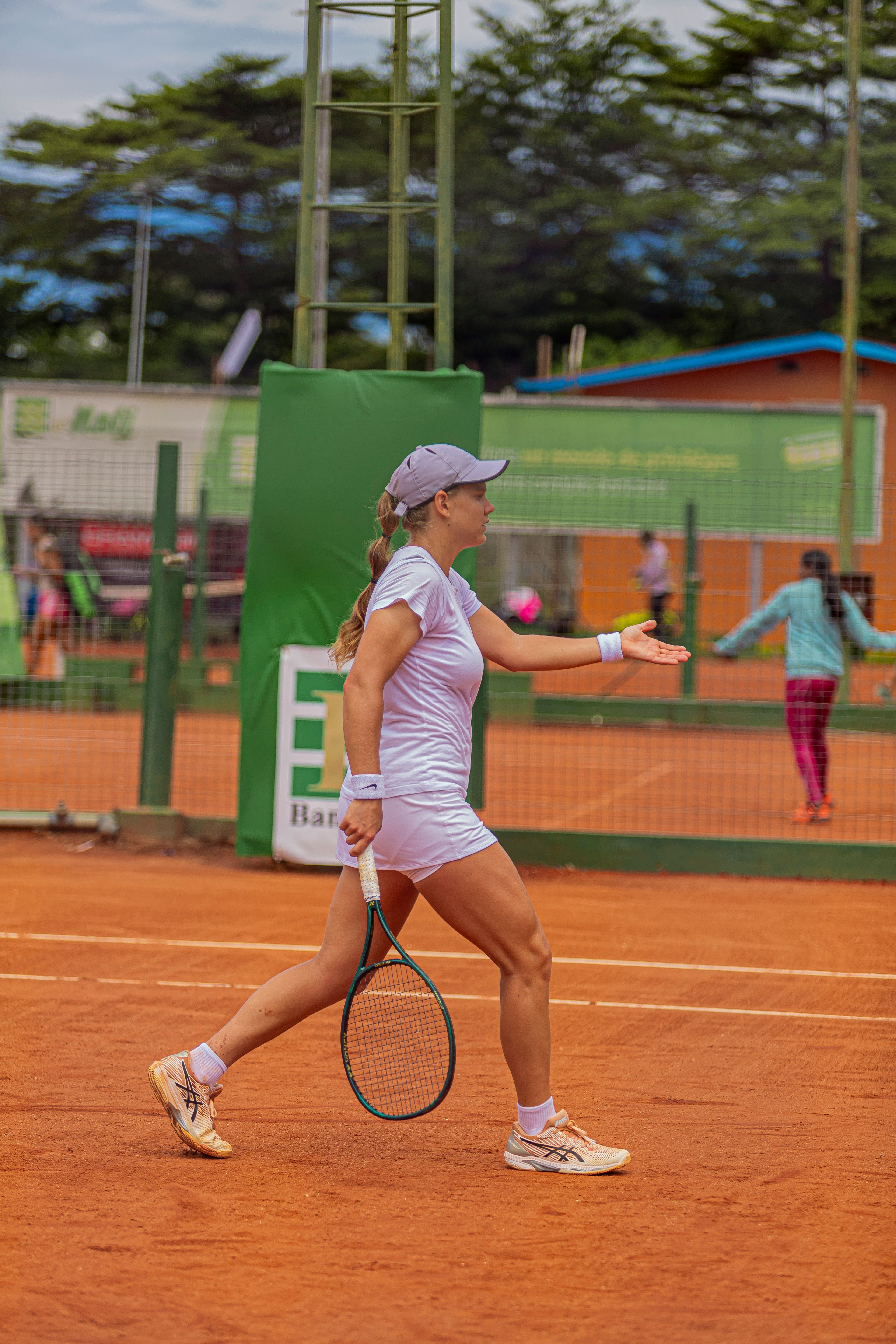 Young female tennis player on an outdoor clay court, preparing to serve during a match.