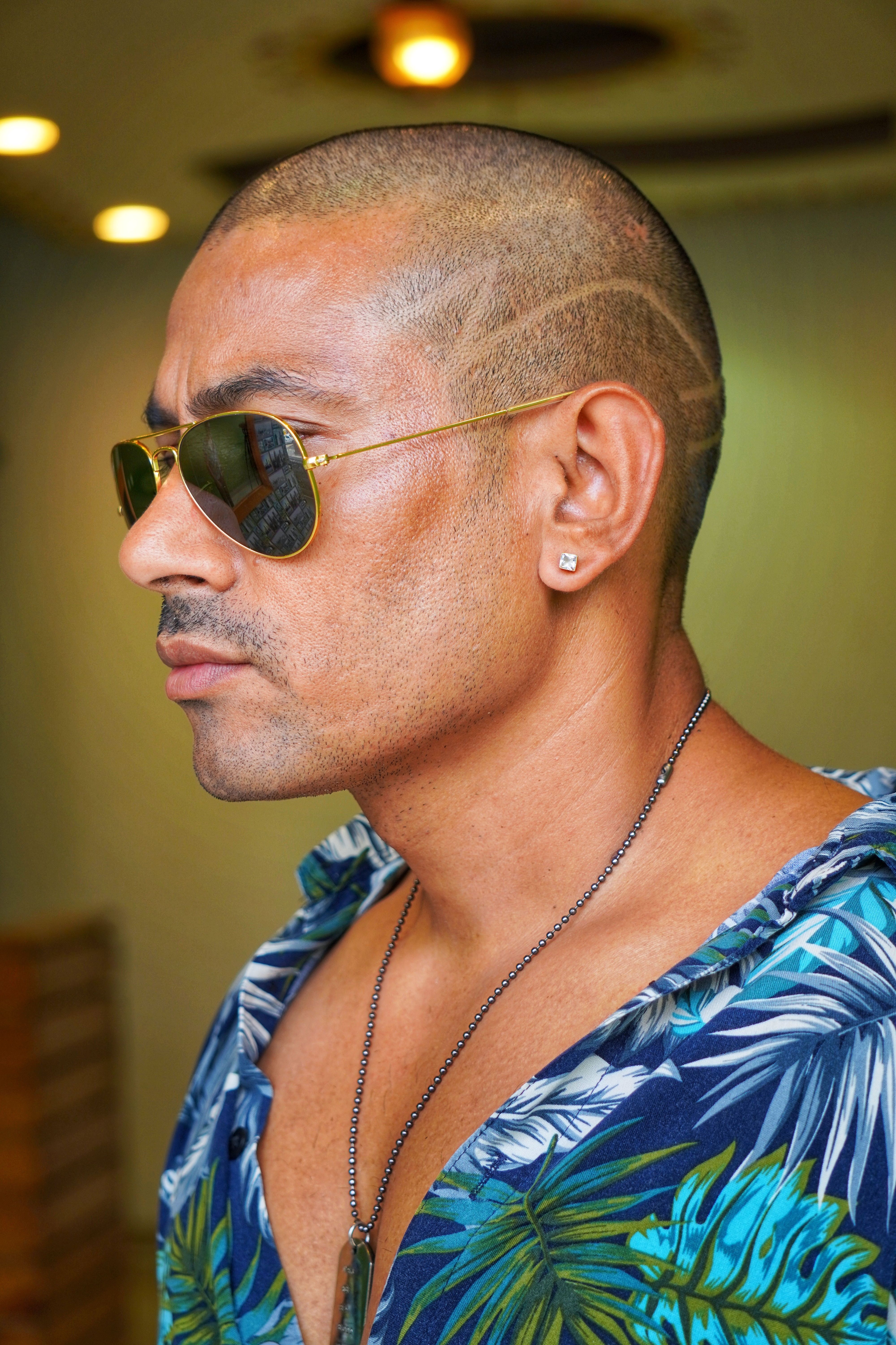 Close-up profile of an adult man wearing sunglasses, showcasing unique haircut and vibrant shirt.