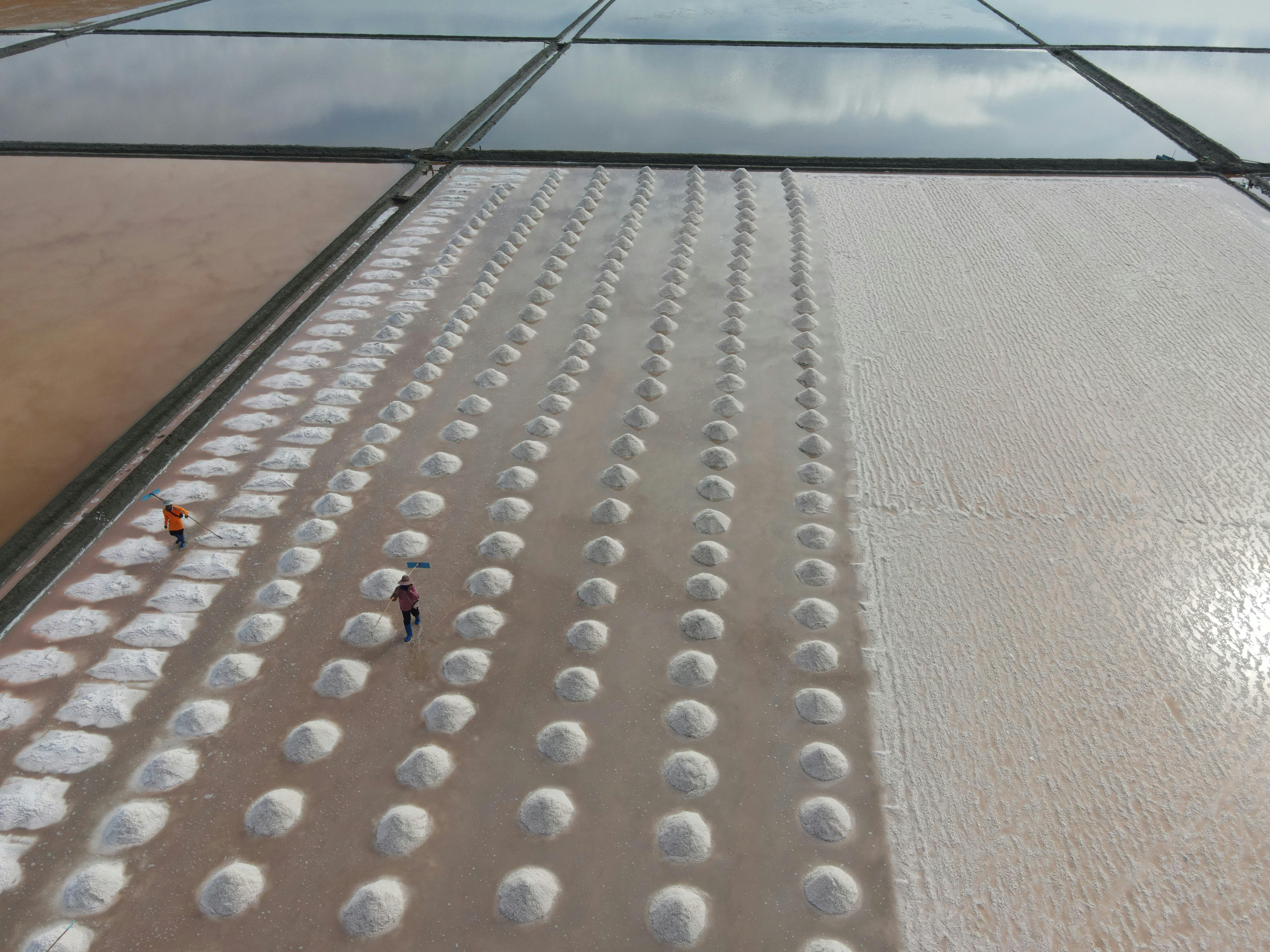 Drone shot capturing workers amidst salt fields in Phetchaburi, Thailand.