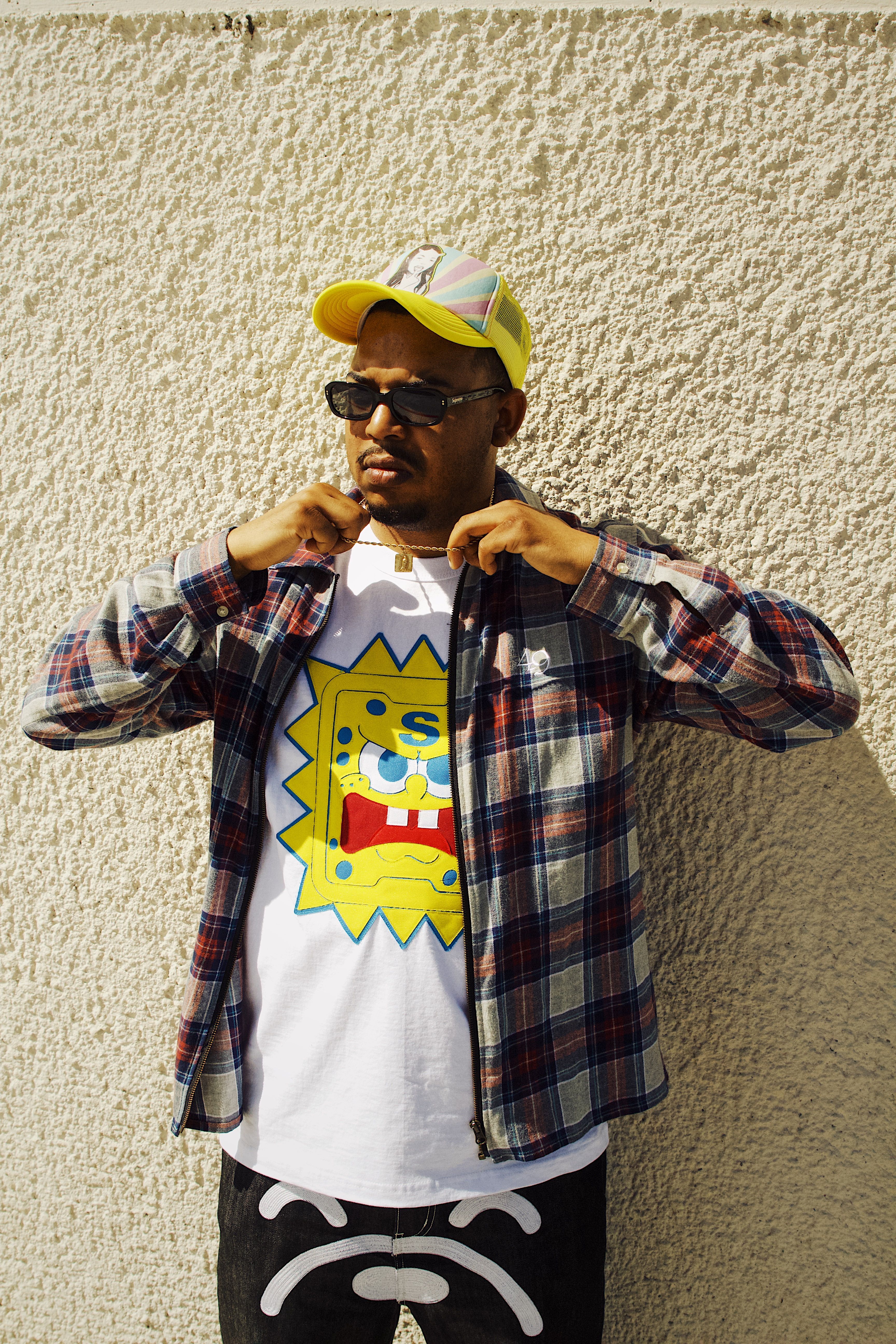 Young man wearing sunglasses and a cartoon print shirt poses in front of a textured wall.