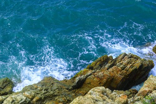 Free A stunning view of rocky coastal formations meeting the vibrant azure sea waves, captured from above. Stock Photo