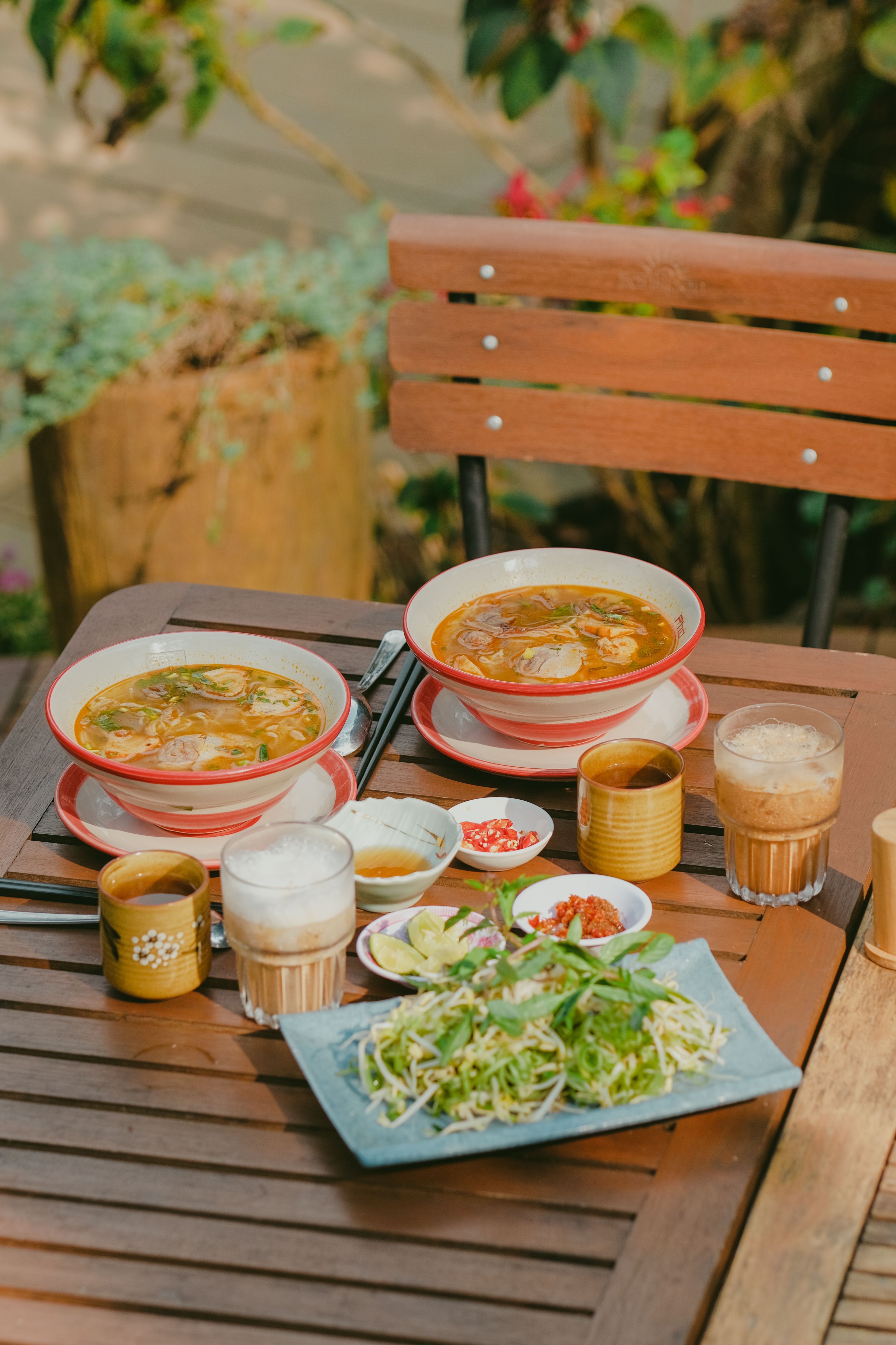 A vibrant Asian noodle soup meal set on an outdoor table with beverages.