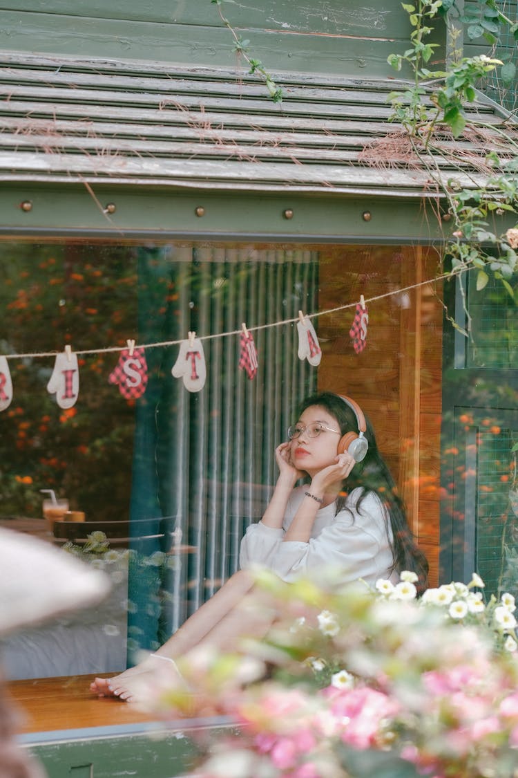 Teenage Girl Sitting In The Window And Listening To Music On Headphones 