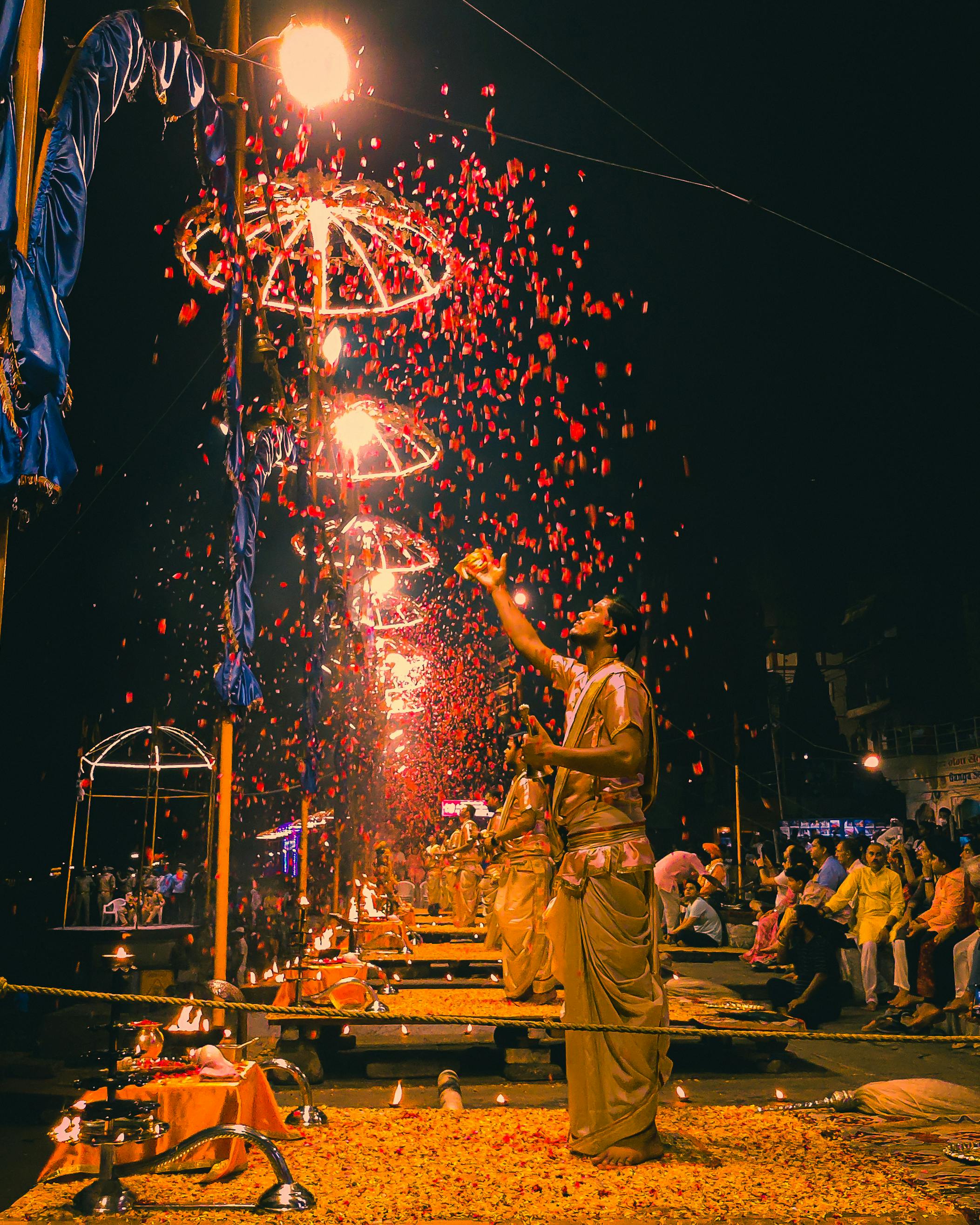 Ganga Aarti in Varanasi with priests performing ritual and vibrant flower petals under illuminated structures.
