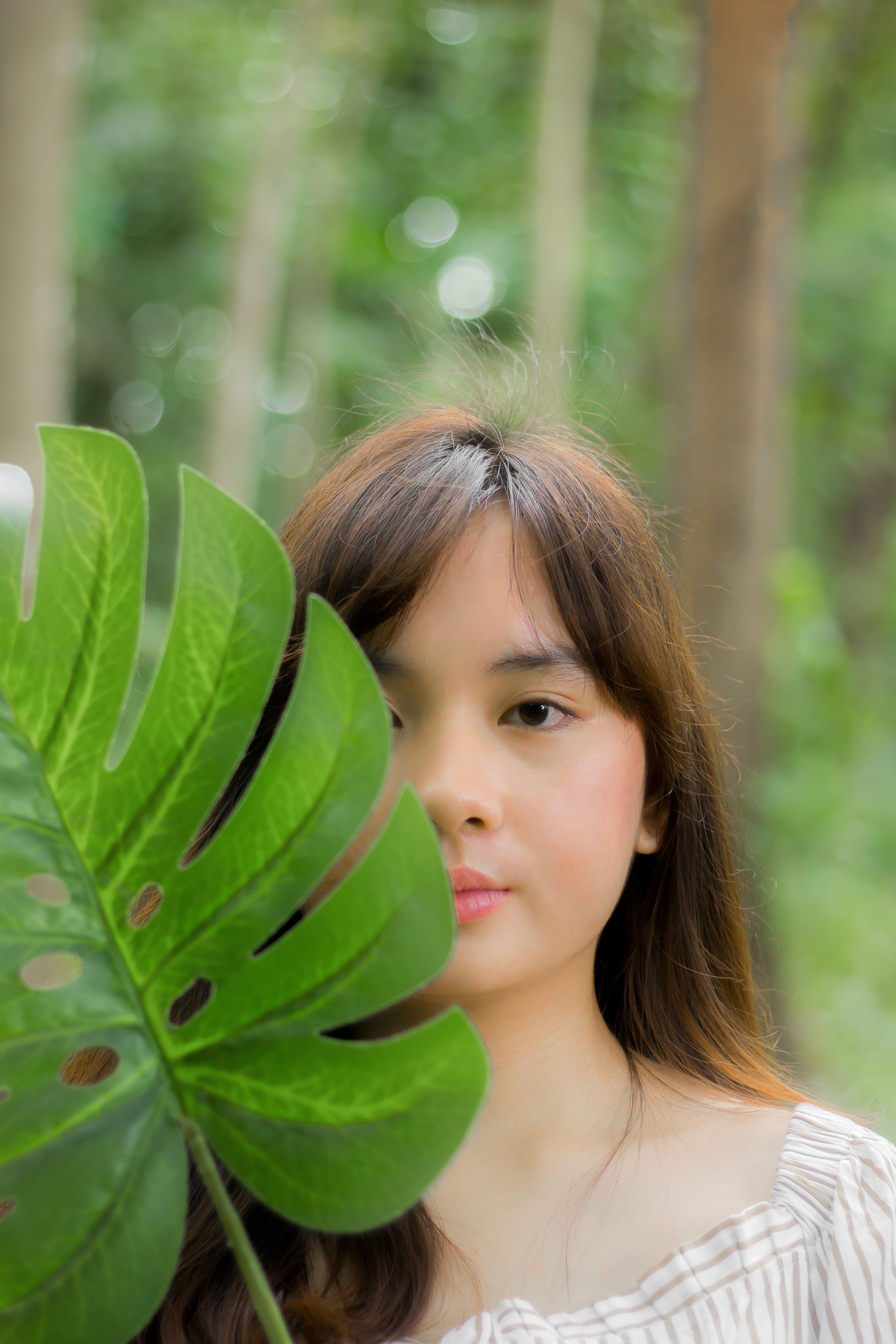 A woman holding a large leaf in front of her face free stock photo