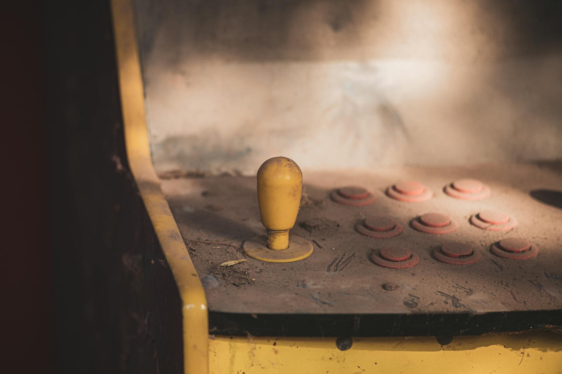 Close-up of a dusty vintage arcade machine control panel with joystick and buttons, evoking nostalgia.