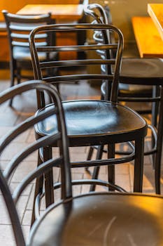 Close-up of black cafe chairs arranged neatly, showcasing cozy atmosphere with warm lighting.