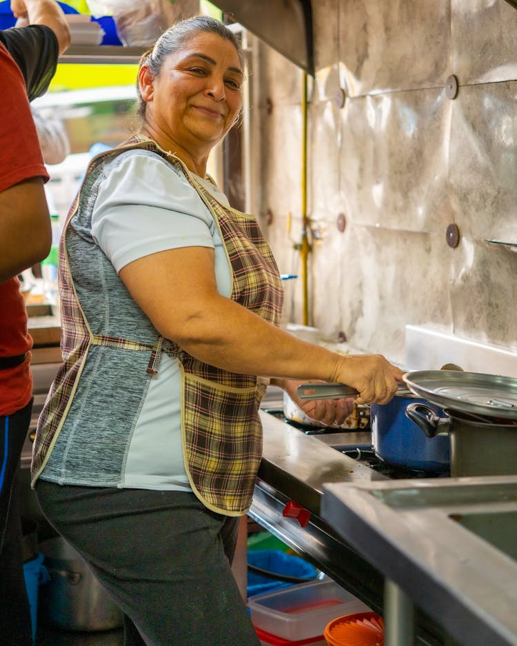 Woman Wearing An Apron Washing Dishes In A Sink 