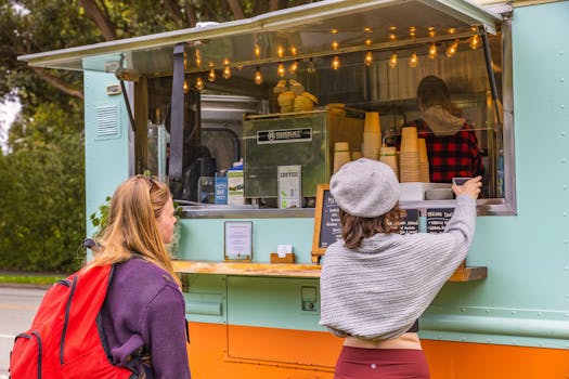 Two women stand at a food truck ordering coffee on a bright day.