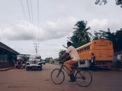 Cyclist navigating through urban traffic with cars and a bus on a cloudy day.