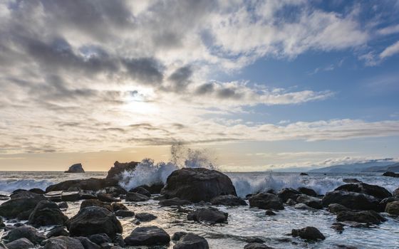 A stunning view of waves splashing against rocks under a vibrant dawn sky, capturing the beauty of the seascape.