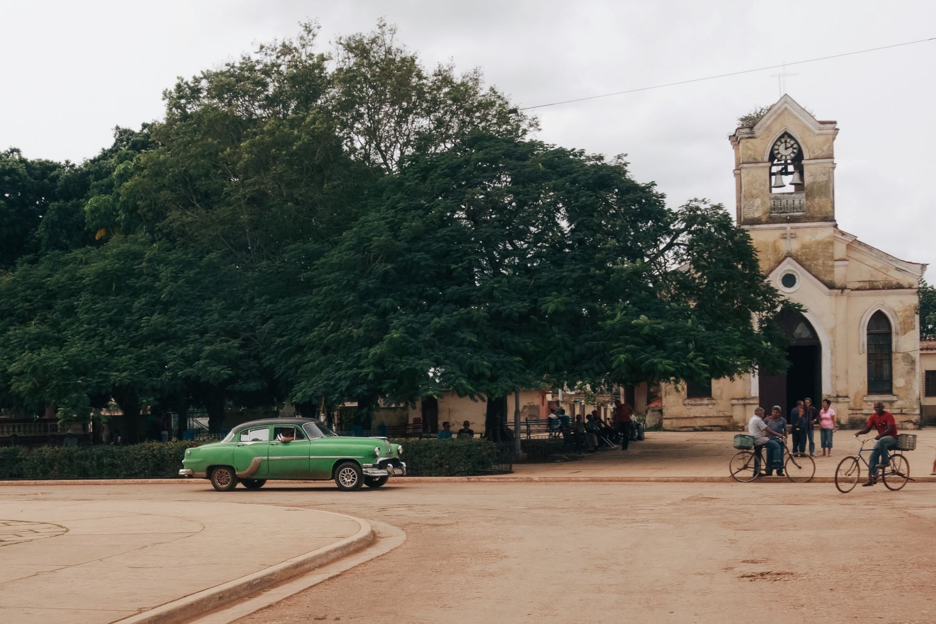 Classic green car in urban Havana with colonial church and city life.