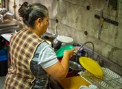 Adult woman performing daily chores in a kitchen, washing dishes at a sink.