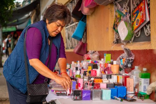 Free A woman arranges colorful cosmetics at an outdoor market stall, promoting local shopping culture. Stock Photo