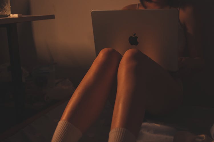 A Woman Sitting On The Bed With A Laptop 