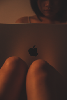 A woman using a laptop with a glowing Apple logo in a dimly lit room.