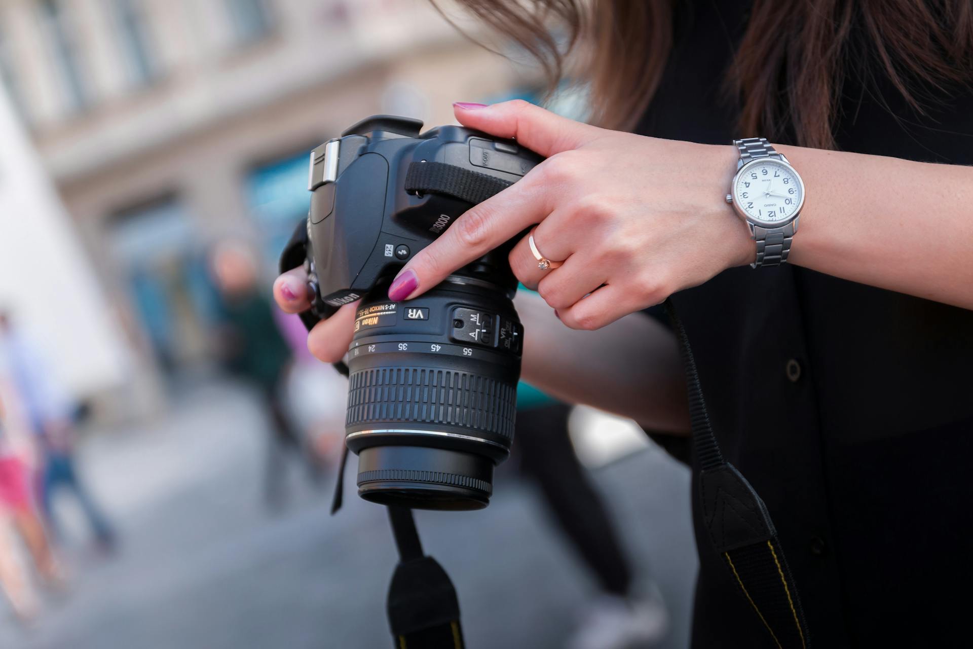 A woman adjusting a DSLR camera outdoors, focusing on her hands and device. Perfect for photography themes.