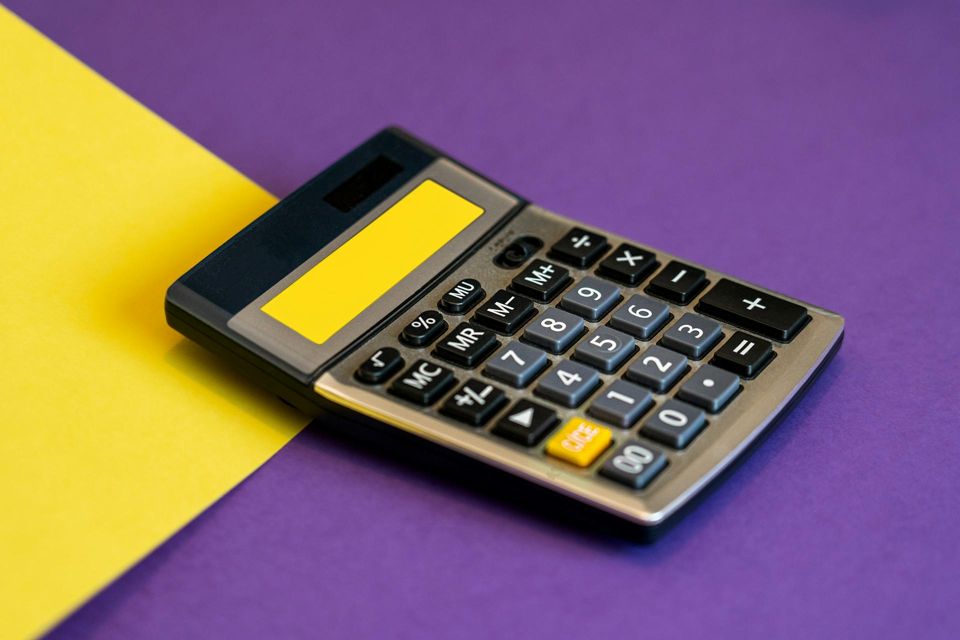 A calculator on vibrant yellow and purple background representing business finance.