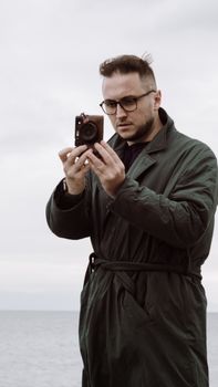 A man stands by a seaside capturing photos with a camera, featuring a serene ocean background.