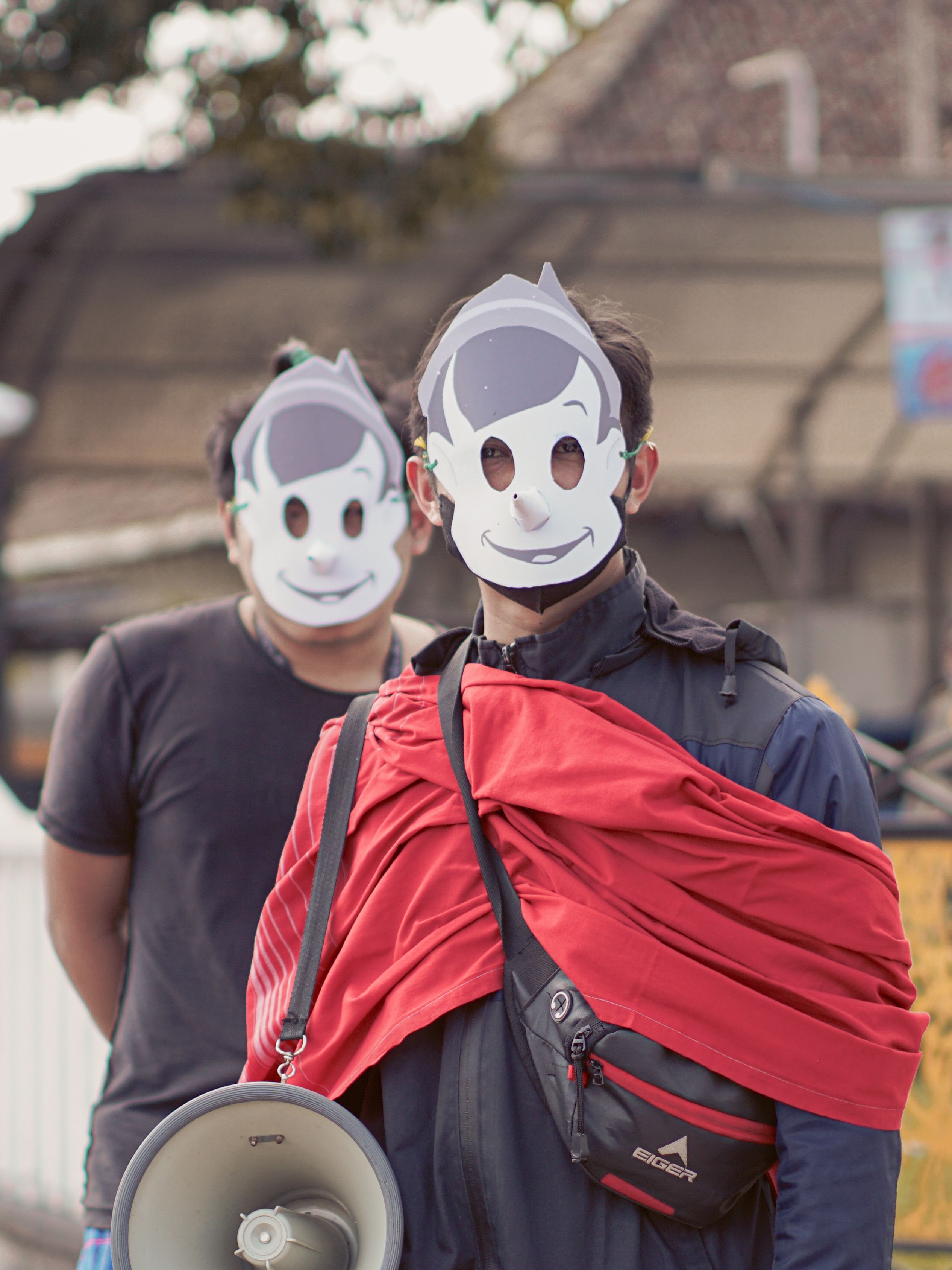 Two people in a parade wear cartoon masks and carry a megaphone, creating a festive atmosphere.