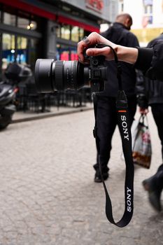 Close-up of a hand holding a camera on a city street, capturing urban life.