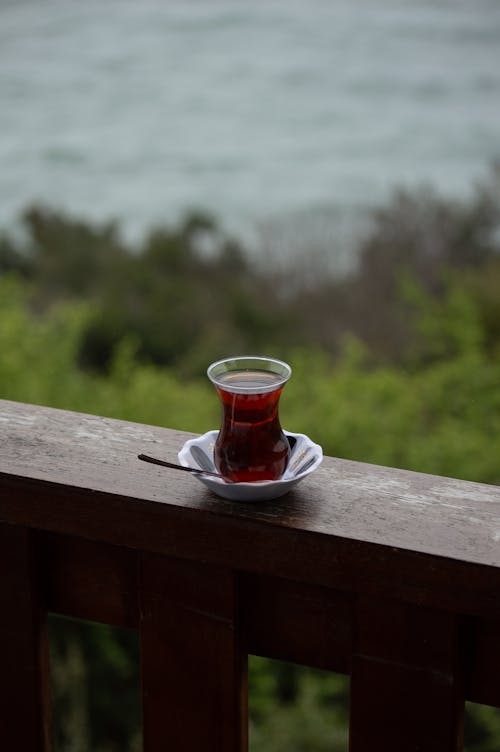 A Glass of Tea on a Wooden Balustrade with the View of a Body of Water in the Background 
