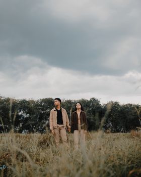 Stylish couple walking in a serene Dutch countryside on a cloudy day.