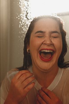 A woman with eyes closed, laughing joyfully under shower spray indoors.