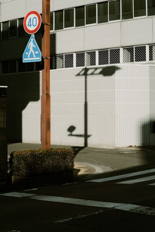 Free Urban street corner with shadows of lamp posts and traffic signs on a building wall. Stock Photo